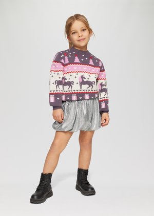 Sweter ma kolorowy splot z wzorami jednorożców, drzew i serc. Połączony z błyszczącą srebrną plisowaną spódnicą i czarnymi butami.