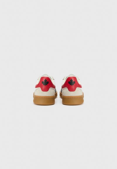 Sneakers med en beige overdel, røde hælpaneler og sort ahornblad-logo. Har en gummisål og en struktureret ruskindsfinish.