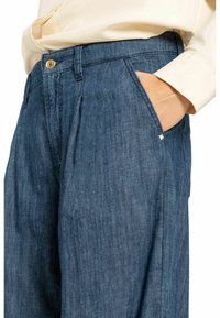 Denim broek in een donkerblauwe kleur, met een knoopsluiting, zijzakken en een relaxte pasvorm met een subtiele textuur. Verfraaid met kleine hardware details.