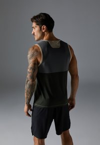 Sportstanktop i mørkegrøn og grå, med et kontrastpaneldesign, rund halsudskæring og struktureret stof. Shorts i marineblå.