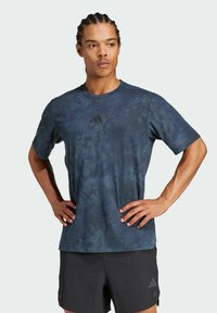 Camiseta deportiva de manga corta, de color azul oscuro, con un acabado texturizado y un patrón, y un pequeño logo negro en el pecho. Combinada con pantalones cortos negros.