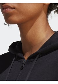 Svart zip-up hoodie med mjuk tygstruktur och dragsko, med en närbild av kragen och detaljerna vid halsringningen.