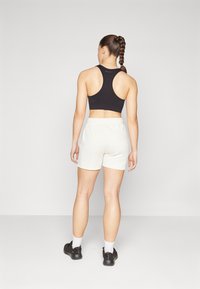Crna sportska bralette bez rukava uparena s bijelim sportskim šortsevima, izrađena od meke tkanine, s opuštenim krojem, i nosi se s tamnim tenisicama.