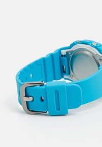 Cinturino per orologio in silicone blu con superficie texturizzata, fibbia in acciaio inossidabile e dettagli con fondo dell'orologio arrotondato. Design semplice e funzionale.