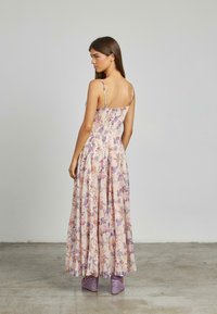 Bloemenmaxi-jurk met dunne bandjes, in pastelkleuren van crème, paars en roze. Lichtgewicht stof met geplooide details, die tot aan de enkels valt.