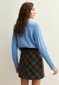 Pull en tricot de couleur bleu clair à manches longues, associé à une jupe à carreaux marron avec des accents bleus et une ceinture noire.