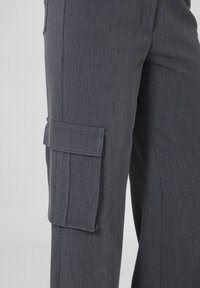 Grijze cargobroek met een gestructureerde stof, wijde pijpen en een zijpatchzak met klep sluiting voor extra functionaliteit.