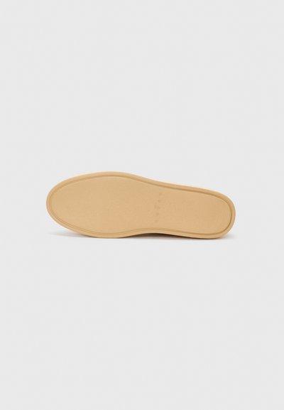 Semelle d'une chaussure, matériau en caoutchouc, couleur beige clair, texture lisse, forme arrondie, motifs décoratifs subtils sur la surface.