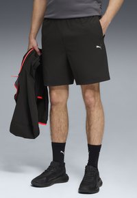 Juodi sportiniai šortai, pagaminti iš lengvos medžiagos, su elastinga juosta ir mažuoju baltu logotipu. Apsirengti su juodais sportiniais bateliais ir kojinėmis.