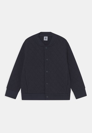 Veste matelassée bleu marine avec boutons-pression, poignets et ourlet côtelés, col rond et manches longues, à plat sur fond blanc.