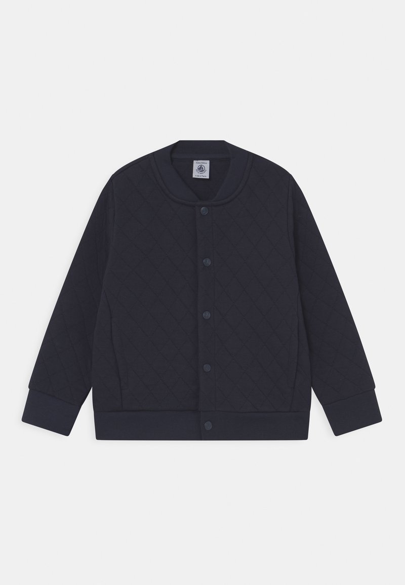 Námořnická modrá prošívaná bunda s patentkami, žebrovanými manžetami a lemem, kulatým výstřihem a dlouhými rukávy, položená na bílém pozadí.