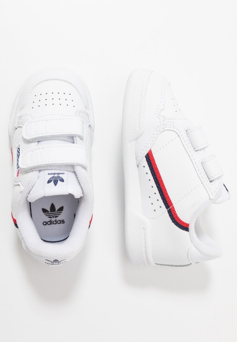 Białe sneakersy Adidas dla malucha z czerwonymi i granatowymi paskami, dwoma paskami na rzepy oraz perforacjami zapewniającymi wentylację, widoczne z góry i z boku.