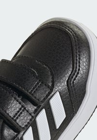 Crne sintetičke tenisice s teksturiranom površinom, bijelim akcentima i tri pruge, pričvršćene čičak trakama.