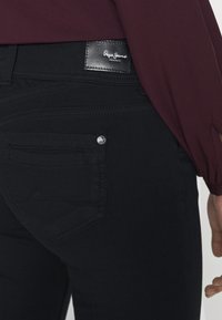 Svarta jeans med strukturerad textil, en liten bakficka och en svart läderlapp med varumärket. Elegant, figursydd design med sömnadsdetaljer.