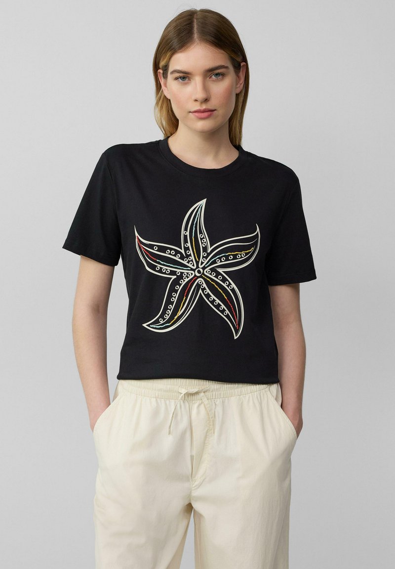 Zwarte cropped t-shirt met een zeesterontwerp in wit, rood en blauwe accenten. De stof lijkt zacht met een ronde hals en korte mouwen.