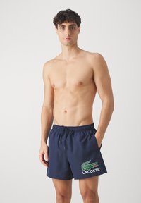 Shorts de bain bleu marine en tissu léger, dotés d'une taille à cordon de serrage et d'un logo crocodile vert Lacoste sur la jambe gauche.