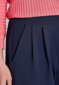 Marineblauwe geplooide broeken gecombineerd met een gestructureerde koraalkleurige ribbeltrui, met een soepele stof en zijzakdetails.