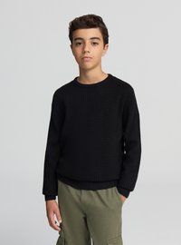 Maglione nero a maglia testurizzata con scollo rotondo, maniche lunghe e polsini a coste, abbinato a pantaloni cargo larghi verde oliva.