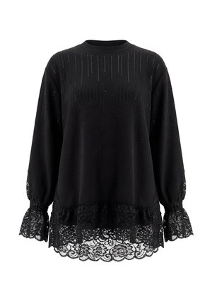 Blusa nera a maniche lunghe con motivo a pois verticale, rifinitura in pizzo sui polsini e sull'orlo e scollo tondo su sfondo semplice.