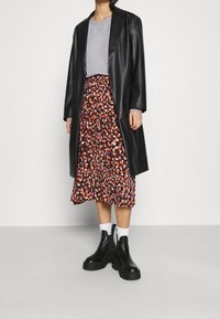 Cappotto lungo in finta pelle nera, t-shirt grigia, gonna midi floreale con motivi rossi e bianchi, stivali platform neri, calzini bianchi.