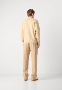 Felpa beige e pantaloni della tuta coordinati, texture morbida, vestibilità rilassata, polsini a coste e dettagli di cucitura sottili, indossati con scarpe bianche.