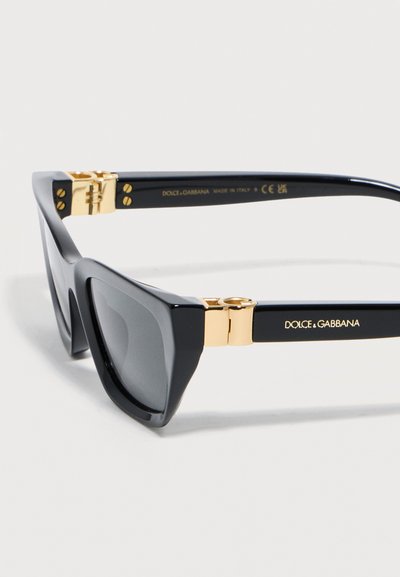 Μαύρα γυαλιά ηλίου cat-eye με σκουρόχρωμους φακούς, χρυσά μεντεσέδες και το λογότυπο "Dolce & Gabbana" στο πλάι του σκελετού.
