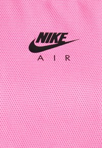 Tejido de malla rosa con el logo de Nike Air en negro. La textura es transpirable y presenta un patrón en forma de cuadrícula.
