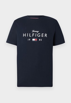 T-shirt a maniche corte blu navy con testo "Tommy Hilfiger 1985" e logo rettangolare rosso, bianco e blu sul petto.