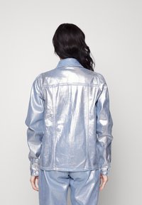 Giacca metallica blu chiaro con design aderente. Presenta un colletto classico, dettagli con bottoni sulle maniche e una texture liscia e lucente.