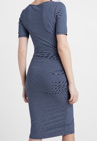 Sukienka bodycon w paski w granatowo-białej kolorystyce, z krótkimi rękawami, dekoltem w serek, elastycznym materiałem oraz detalami marszczenia po bokach.