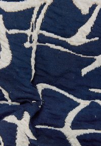 Textil mit navy-blauem Hintergrund und kontrastierenden weißen abstrakten Mustern. Der Stoff hat eine weiche Textur und zeigt an den Rändern leichte Ausfransungen.