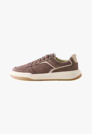 Brun ruskind lavt sneakers med creme-accenter, hvid tyk sål og snørebånd foran på hvidt baggrund.