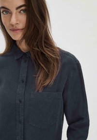 Camicia button-up blu scuro con maniche lunghe, colletto a punta, taschino singolo sul petto e tessuto texture.