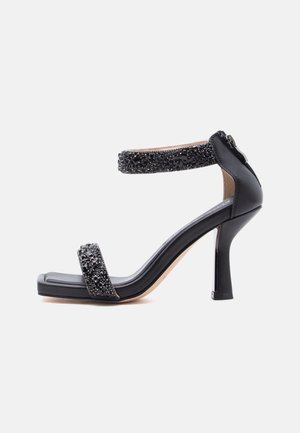 Czarna sandałka na wysokim obcasie z kwadratowym noskiem, dwoma paskami ozdobionymi czarnymi koralikami oraz zamkiem błyskawicznym z tyłu do zapięcia.