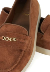 Brown suede loafers with a gold chain accent and a beige rubber sole. Smooth texture with stitched detailing around the upper.