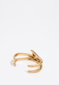 Anillo en tono dorado con un diseño abstracto de garra con dos extremos abiertos. Textura suave y acabado pulido, que destaca los detalles en los acentos.