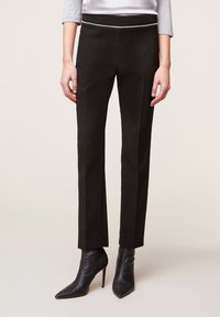 Svarta skräddarsydda byxor med smal passform, med en dekorerad midjebanddetalj och slät tygtextur. Matchas med spetsiga svarta ankelstövlar.