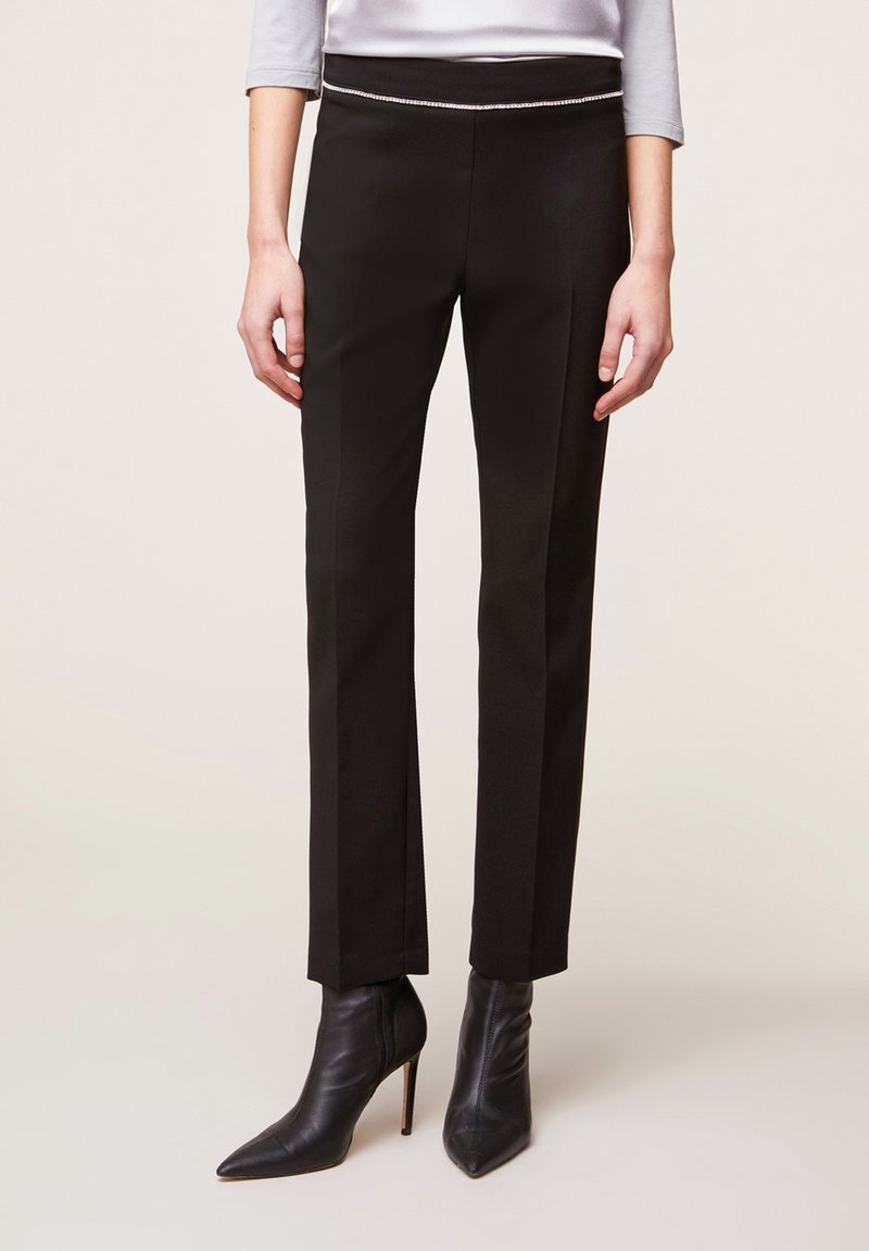 Svarta skräddarsydda byxor med smal passform, med en dekorerad midjebanddetalj och slät tygtextur. Matchas med spetsiga svarta ankelstövlar.