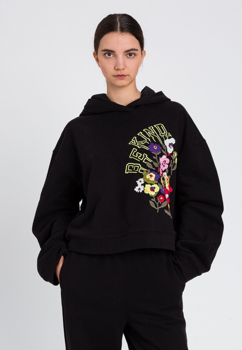 Felpa corta nera in tessuto morbido, con ricamo floreale colorato e testo giallo audace. Vestibilità ampia con cappuccio.
