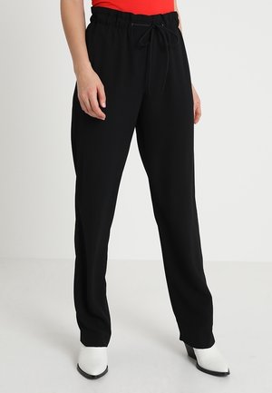 Pantalons noirs légers avec une taille à cordon, coupe ample et texture lisse ; associés à un haut rouge ajusté et des bottes blanches.