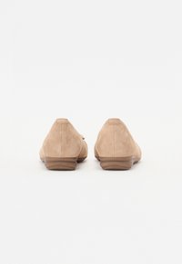 Scarpe in suede color sabbia con punta arrotondata e tacco basso marrone, caratterizzate da una texture liscia e un design semplice senza hardware o accenti aggiuntivi.