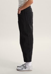 Pantalones de mezclilla negra de corte recto, con bolsillos laterales y costuras visibles. Combinados con zapatos plateados y calcetines blancos.