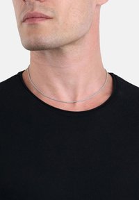 Collar de cadena de plata reposando sobre el cuello, con un delicado diseño metálico redondeado y una textura suave, usado sobre una camisa negra.