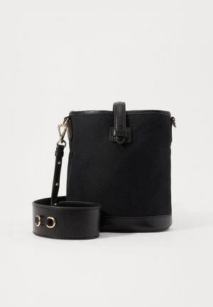 Schwarze zylindrische Bucket-Bag aus Stoff und Leder mit breitem, abnehmbarem Schulterriemen und goldfarbenen Beschlägen vor weißem Hintergrund.