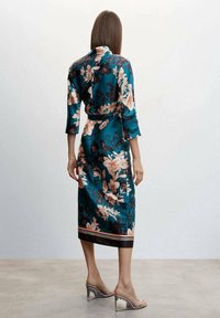 Floral satijnen jurk met een teal basis, driekwart mouwen en een strik taille. Heeft roze en zwarte bloemen, en een zoom die is geaccentueerd met strepen.