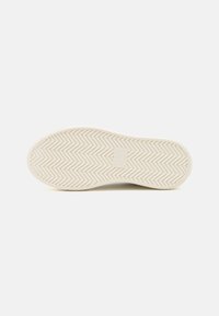 Semelle de chaussure en caoutchouc avec un motif en chevrons, présentant une couleur crème lisse et un logo en relief au centre.