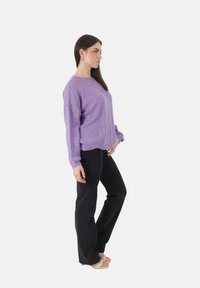 Lavendel gebreide trui met een gestructureerd patroon, ontspannen pasvorm en geribde manchetten, gecombineerd met zwart taps toelopende jeans en beige sandalen.