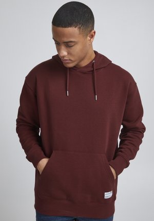 Sweat-shirt à capuche bordeaux en tissu doux, avec une poche kangourou à l'avant, un capuchon avec cordon de serrage et des poignets côtelés. Étiquette de marque minimaliste visible.