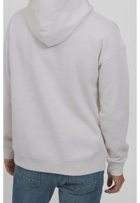 Sweat à capuche en coton blanc à texture douce, doté d'une capuche à cordon de serrage et de poignets côtelés, porté avec un jean en denim bleu.