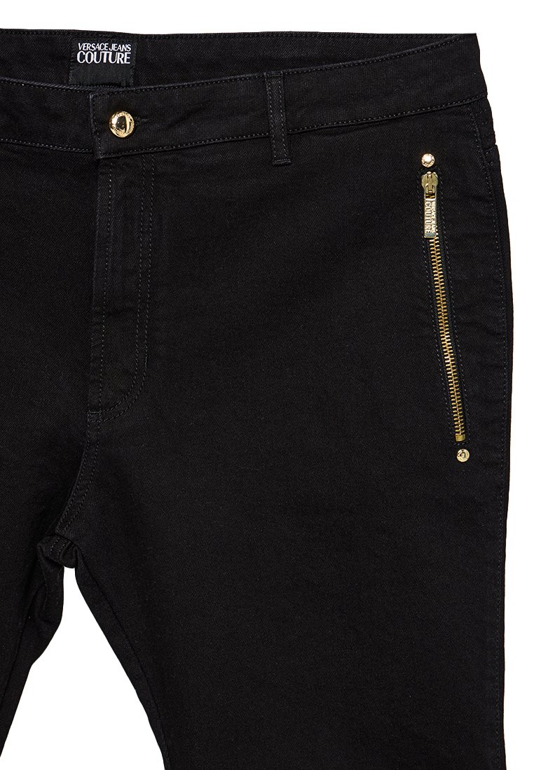 Zwarte denim broek met een gouden ritszak, een gepolijste gouden knoop en een label met "Versace Jeans Couture" op de tailleband.